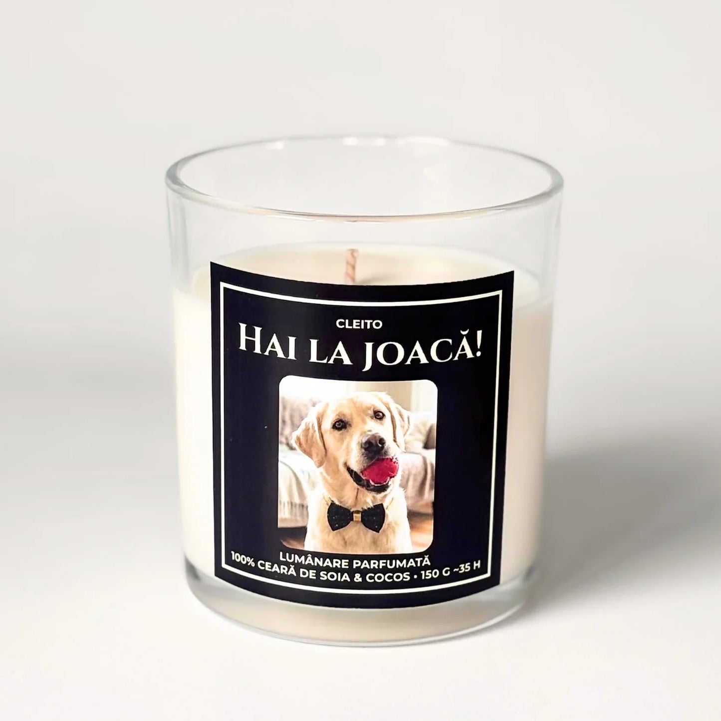 Lumânare parfumată artizanală Cleito din ceară de soia și cocos în pahar de sticlă transparentă, cu etichetă neagră premium. Eticheta prezintă o ilustrație adorabilă a unui câine labrador Golden Retriever cu papion și minge, sub textul alb „Hai la Joacă!”.