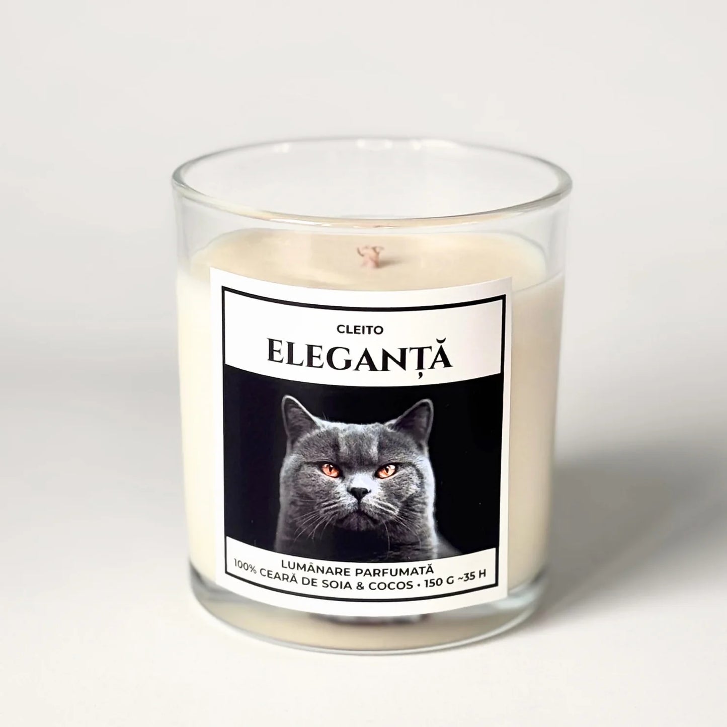 Lumanare parfumata artizanala Cleito in recipient de sticla, cu eticheta alba ce contine o fotografie cu o pisica British Shorthair mândră cu ochi aurii și mesajul 'ELEGANȚĂ'. Ceară de soia și cocos turnata manual.