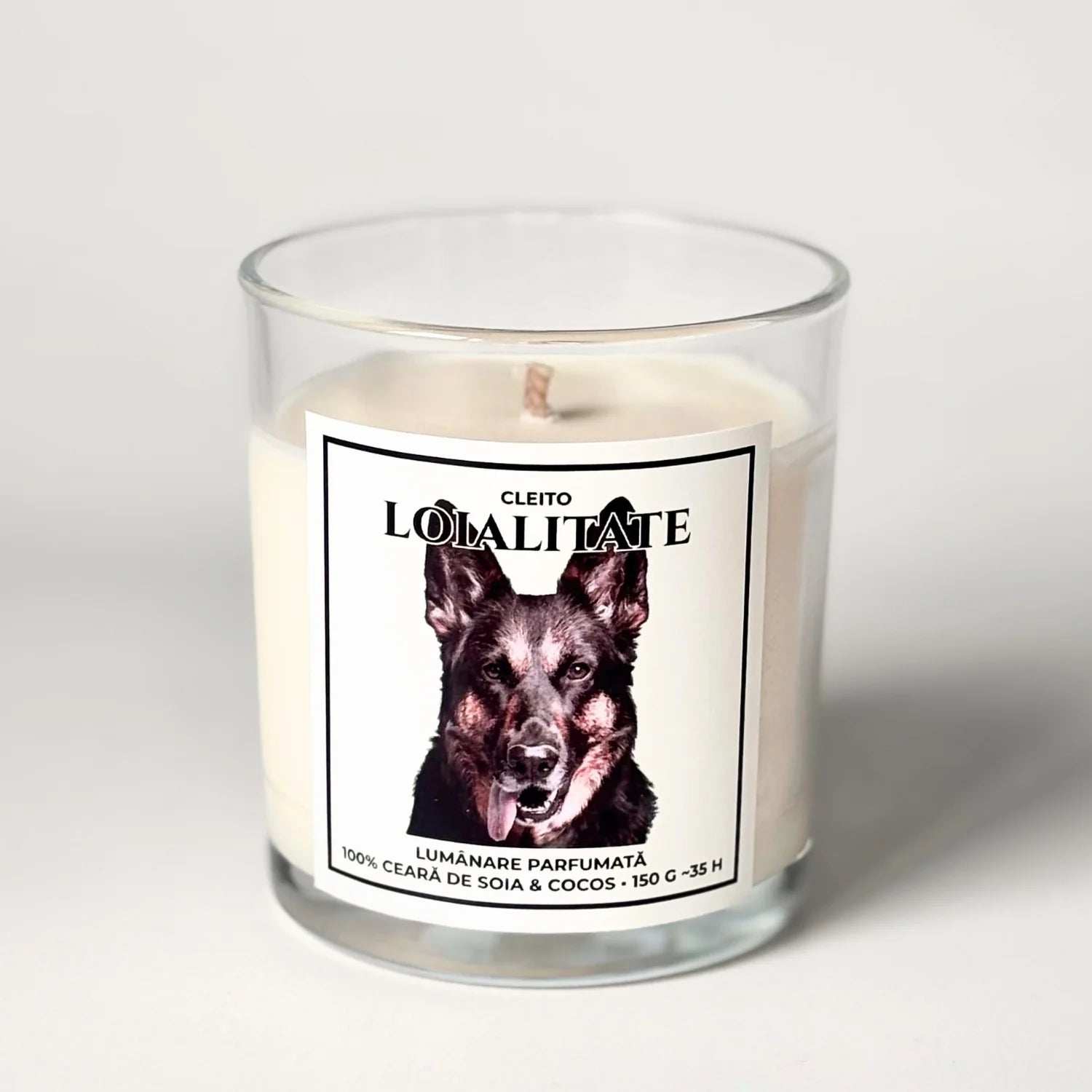 Lumânare parfumata naturala handmade Cleito „Loialitate” în recipient de sticlă transparentă. Eticheta albă conține portretul detaliat al unui Ciobănesc German și textul „LOIALITATE”. Produs din ceară naturală de soia și cocos, 150g.