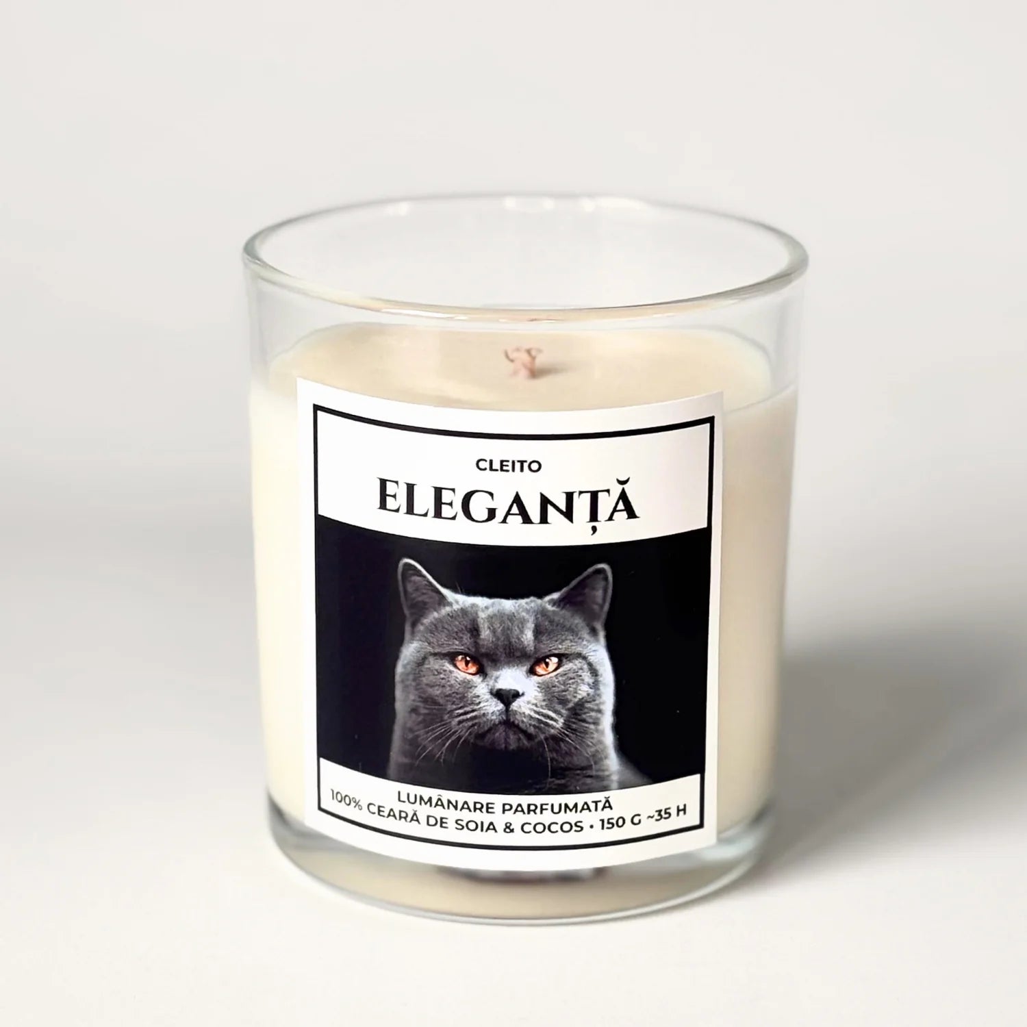 Lumanare parfumata artizanala Cleito in recipient de sticla, cu eticheta alba ce contine o fotografie cu o pisica British Shorthair mândră cu ochi aurii și mesajul 'ELEGANȚĂ'. Ceară de soia și cocos turnata manual.