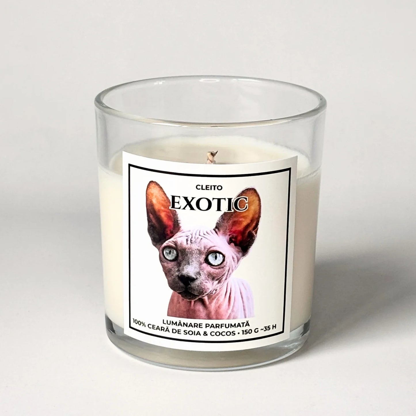 Lumanare parfumata artizanala Cleito in recipient de sticla, cu eticheta alba ce contine o fotografie cu o pisica Sphynx hipnotizanta cu ochi albastri si mesajul 'EXOTIC'. Ceară de soia și cocos turnata manual
